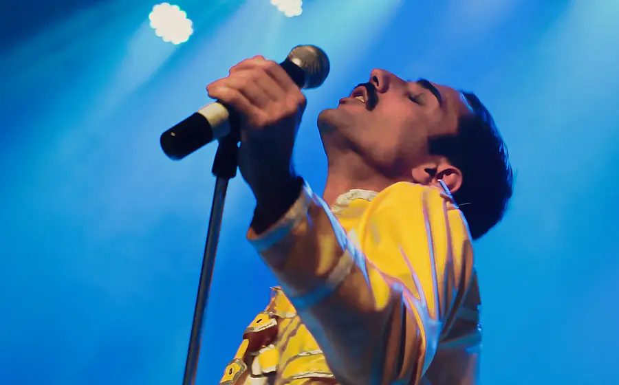 Sänger in gelber Jacke hält ein Mikrofon auf einer blau beleuchteten Bühne bei einer Live-Performance