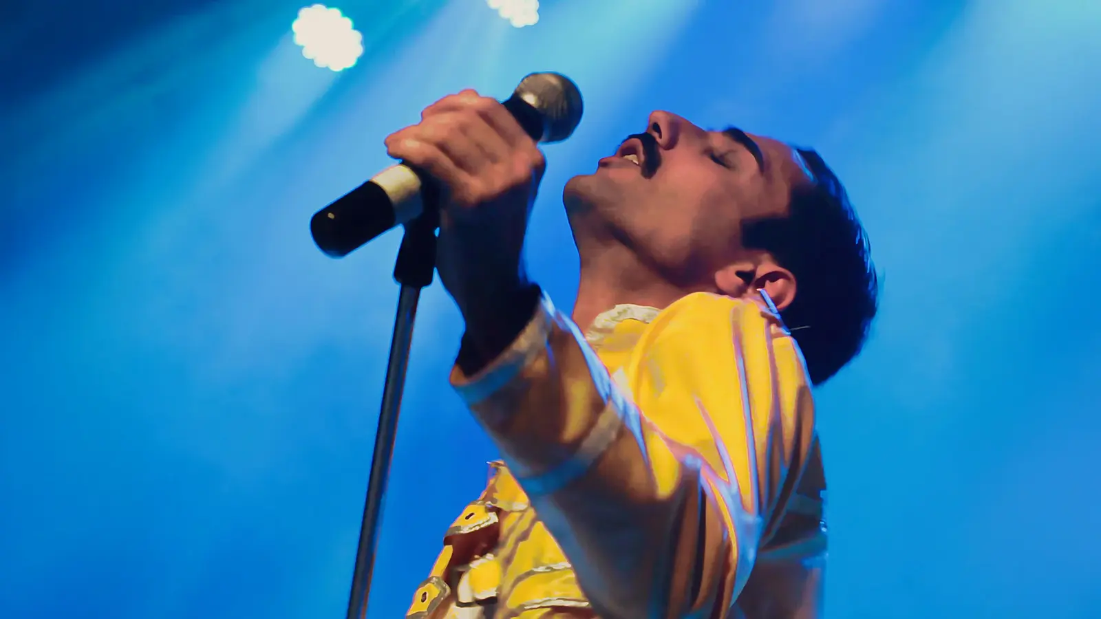 Sänger in gelber Jacke hält ein Mikrofon auf einer blau beleuchteten Bühne bei einer Live-Performance