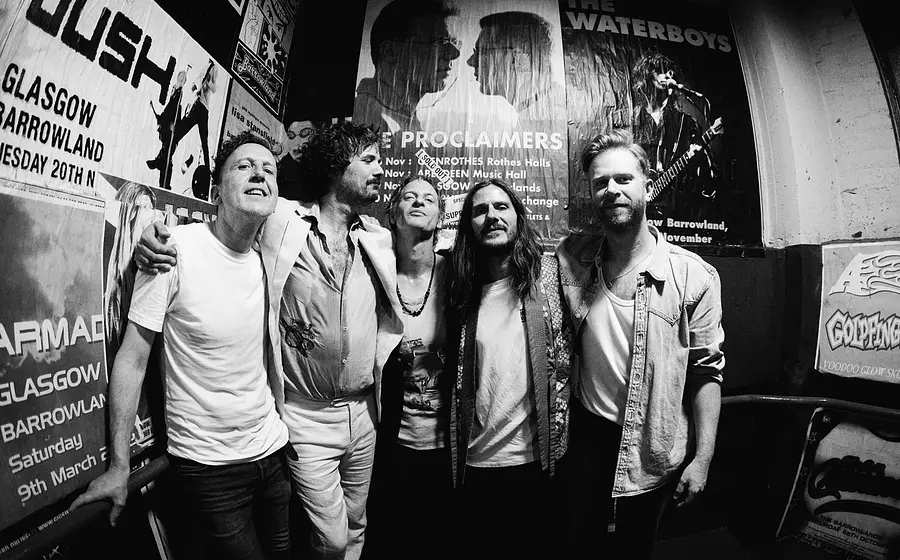 The Temperance Movement, fünfköpfige Rockband aus Glasgow, stehen eng beieinander in einem Backstagebereich mit Konzertplakaten an den Wänden, schwarz-weißes Gruppenfoto – Pressebild zur „Let It All Out“-Tour