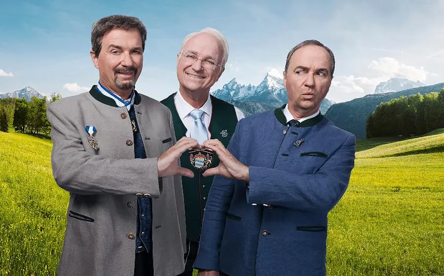 Eine Collage aus drei Fotos, mit Wolfgang Krebs und zwei Darstellern von Markus Söder und Edmund Stoiber auf einer Wiese mit Bergen im Hintergrund