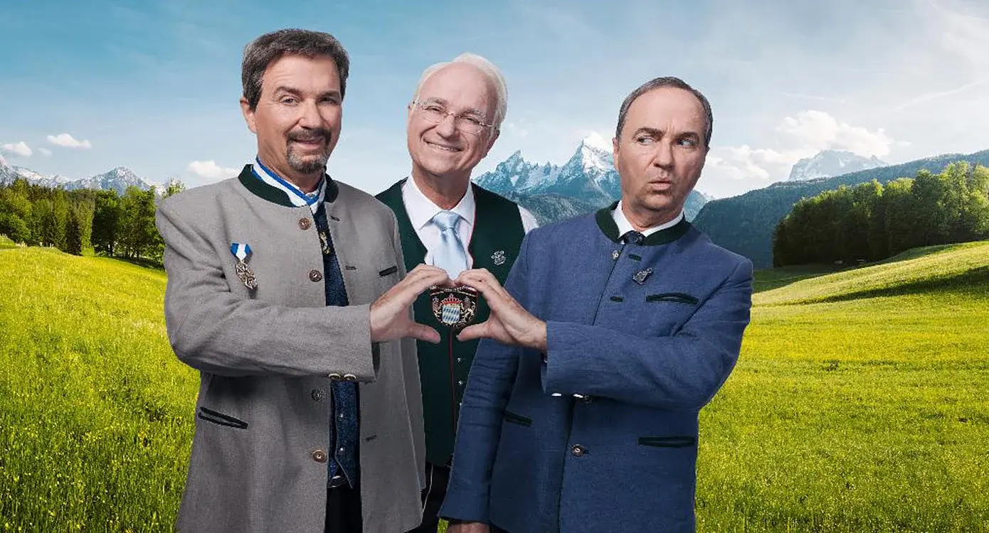 Eine Collage aus drei Fotos, mit Wolfgang Krebs und zwei Darstellern von Markus Söder und Edmund Stoiber auf einer Wiese mit Bergen im Hintergrund