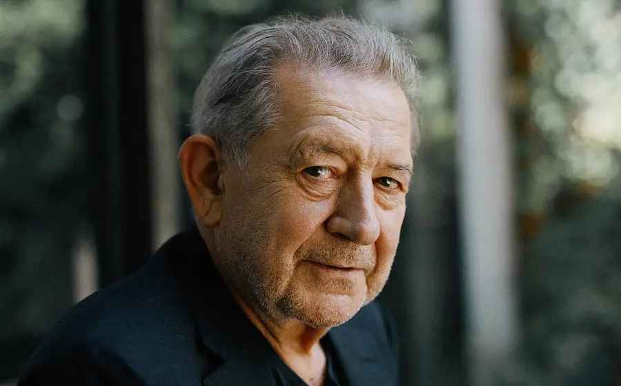 Portrait von André Jung in einem schwarzen Sakko seitlich in die Kamera blickend, der Hintergrund verschwommen