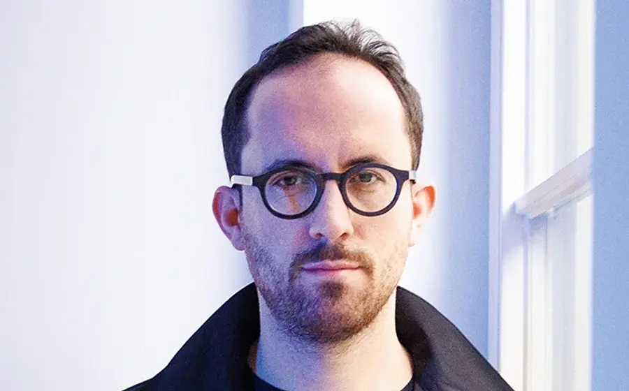 Ein Portrait von Igor Levit mit Brille vor hellem Hintergrund mit weißem Fensterrahmen