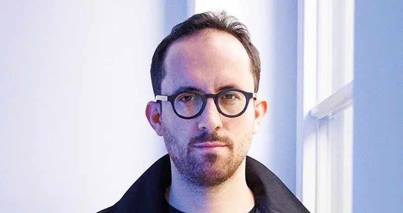 Ein Portrait von Igor Levit mit Brille vor hellem Hintergrund mit weißem Fensterrahmen