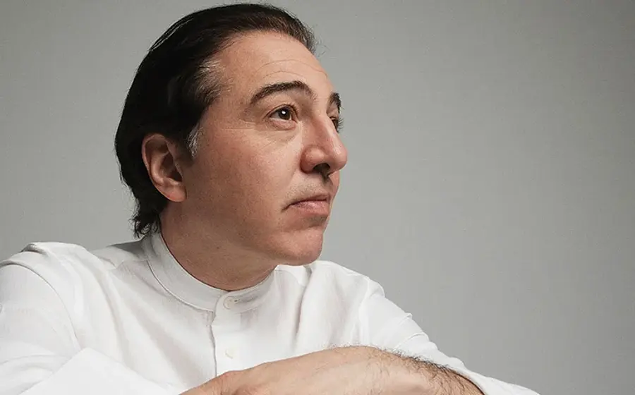 Der Künstöer Fazil Say in weißem Hemd zur Seite blickend, vor hellgrauem Hintergrund
