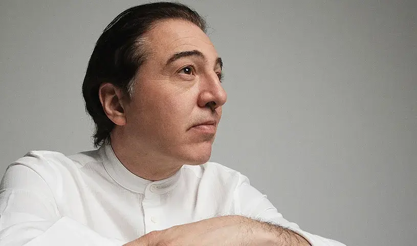 Der Künstöer Fazil Say in weißem Hemd zur Seite blickend, vor hellgrauem Hintergrund