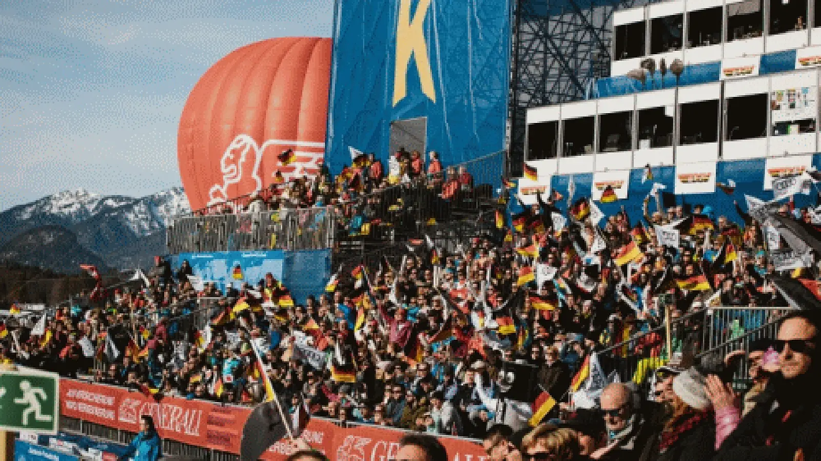 Foto vom Ski-Weltcup in Garmisch-Partenkirchen mit voll besetzten Zuschauertribünen, zahlreichen Deutschlandfahnen im Publikum, großem Kandahar-Ballon und verschneiter Bergkulisse im Hintergrund