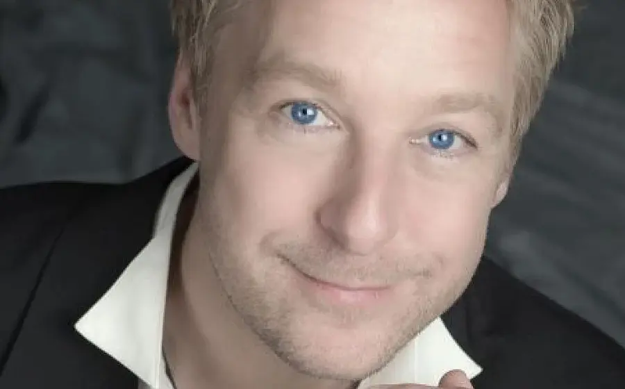 Portrait einer Person mit schwarzem Sakko undweißem Hemdkragen vor grauem Hintergrund