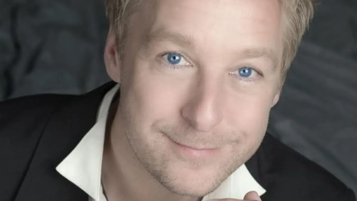 Portrait einer Person mit schwarzem Sakko undweißem Hemdkragen vor grauem Hintergrund