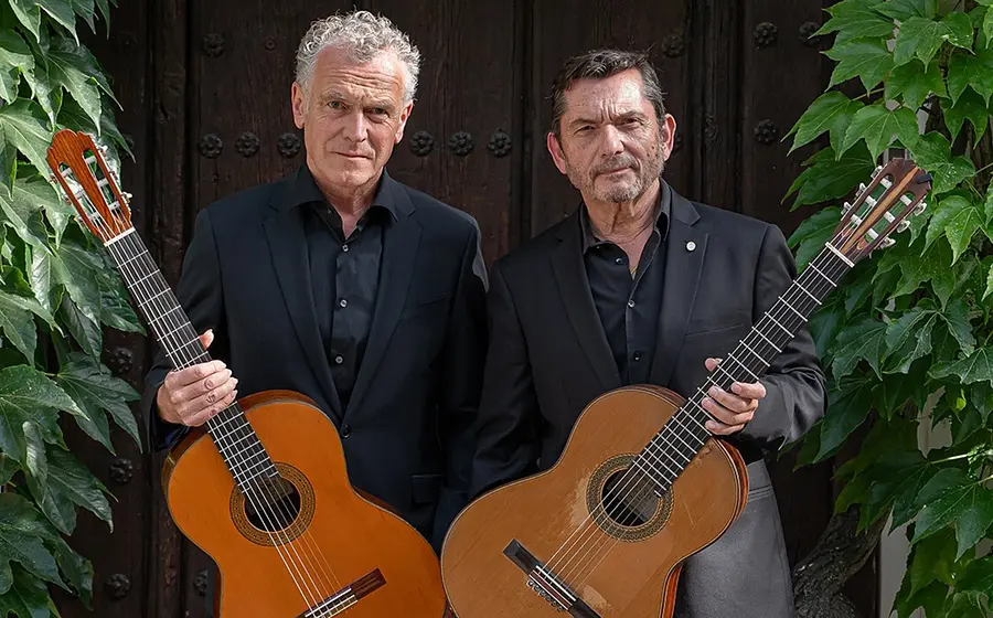 Das Gitarrenduo Wiedermann und GAllardo del Rey mit Gitarren vor einer Holztür, links und rechts im Bild Kletterpflanzen