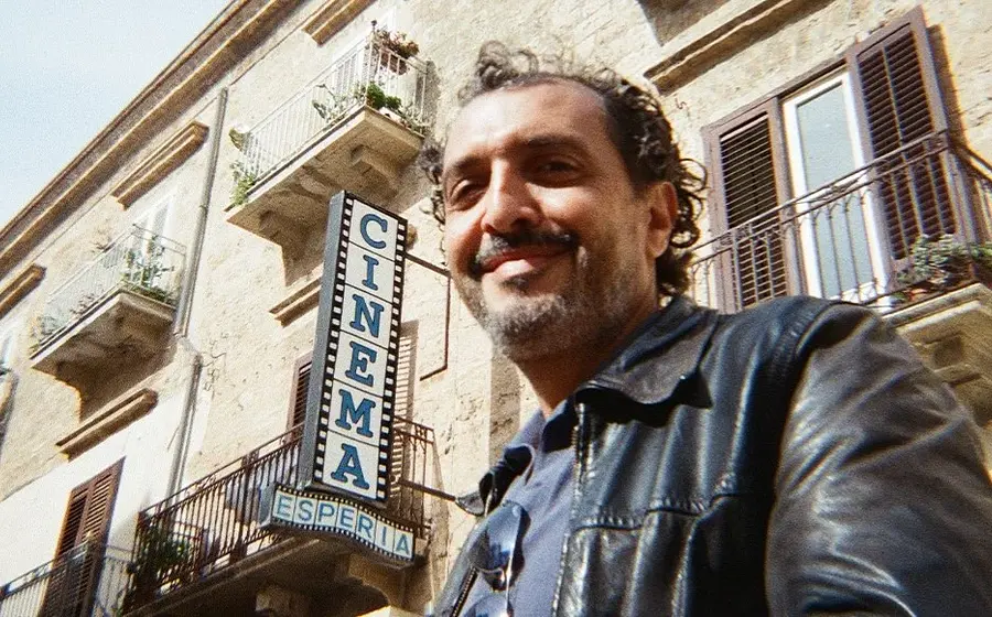 Der Künstler Kid Francescoli steht vor einer altertümlichen Hauswand mit Balkonen sowie einem Schild mit der Aufschrift Cinema