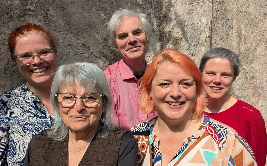 Pressefoto von Weihnachten? Ja bitte! mit fünf Mitwirkenden vor einer Natursteinwand, darunter vier Personen mit Brille und eine Person mit rosa Haaren, in farbenfroher Kleidung und gruppiert für die Kamera.