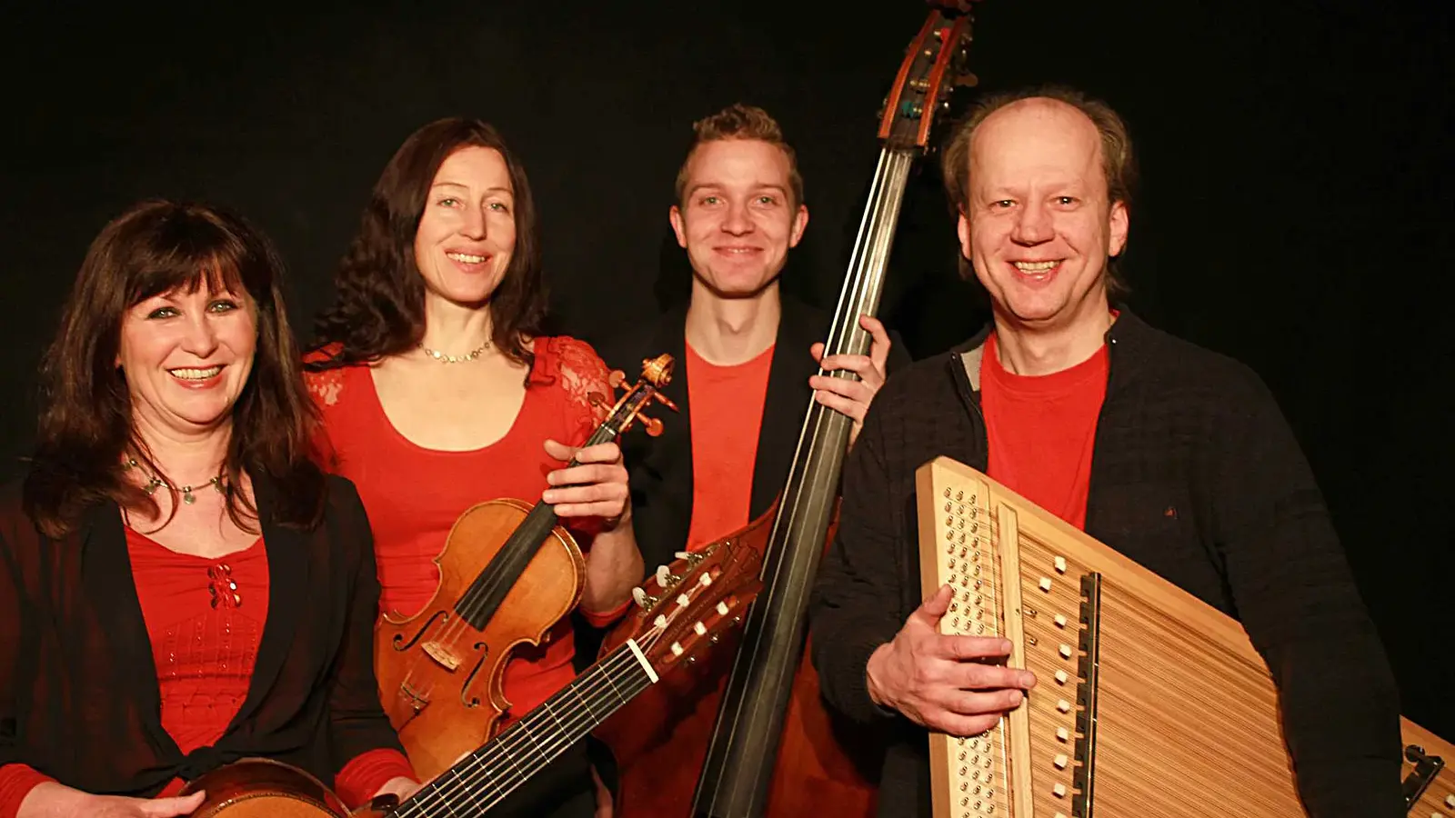 Bandfoto eines Ensembles mit Rudi Zapf und drei Musikerinnen und Musikern vor schwarzem Hintergrund, in rot schwarzen Outfits, mit Instrumenten wie Violine, Gitarre, Kontrabass und Zither in den Händen.