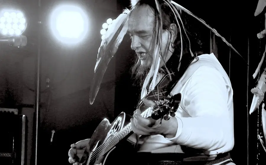 Schwarz-weiss Bild von Willy Michl mit Federschmuck auf dem Kopf und Gitarre auf einer Bühne