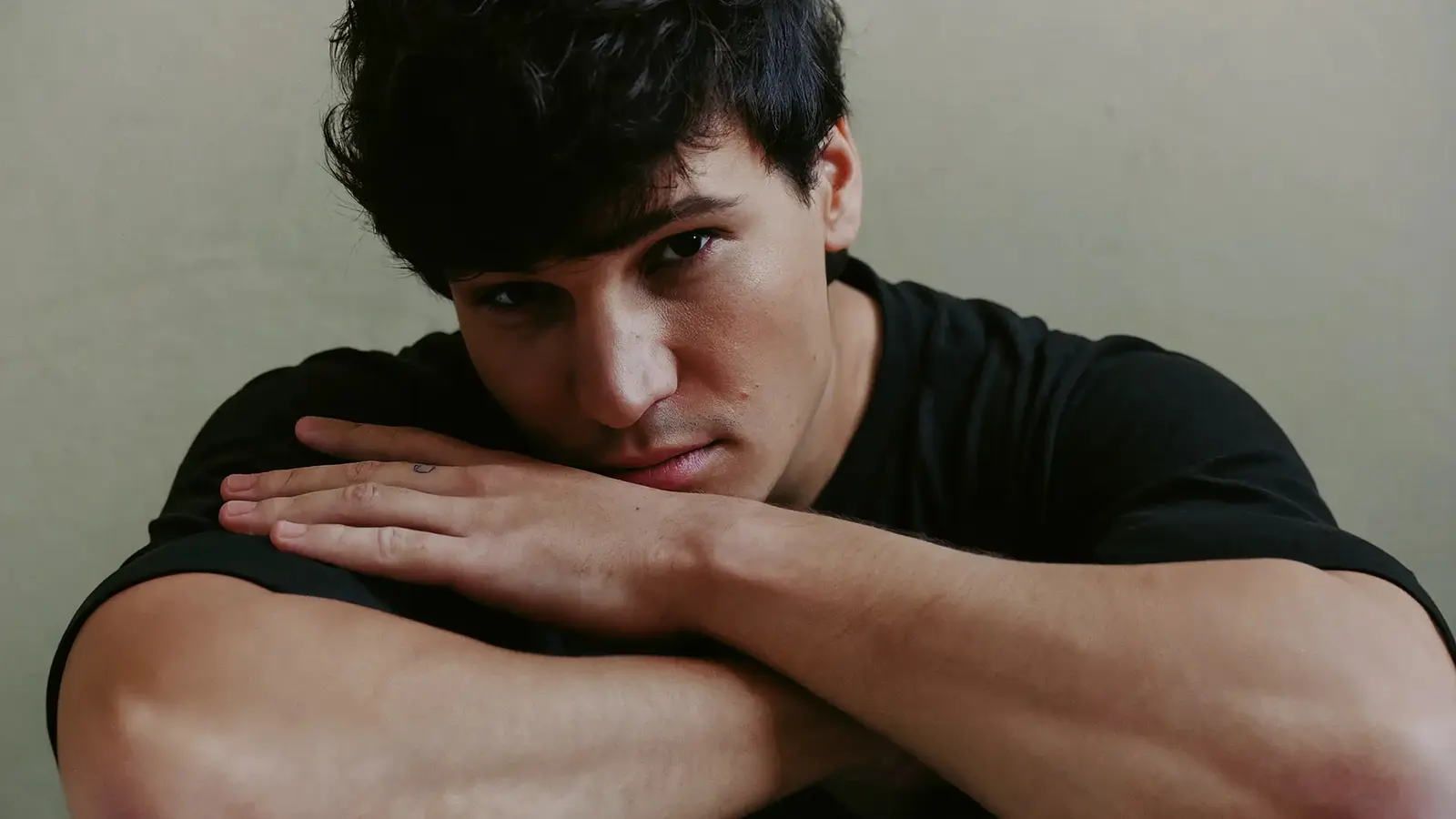Wincent Weiss in schwarzem T Shirt stützt den Kopf auf verschränkte Arme und blickt direkt in die Kamera, vor hellem Hintergrund