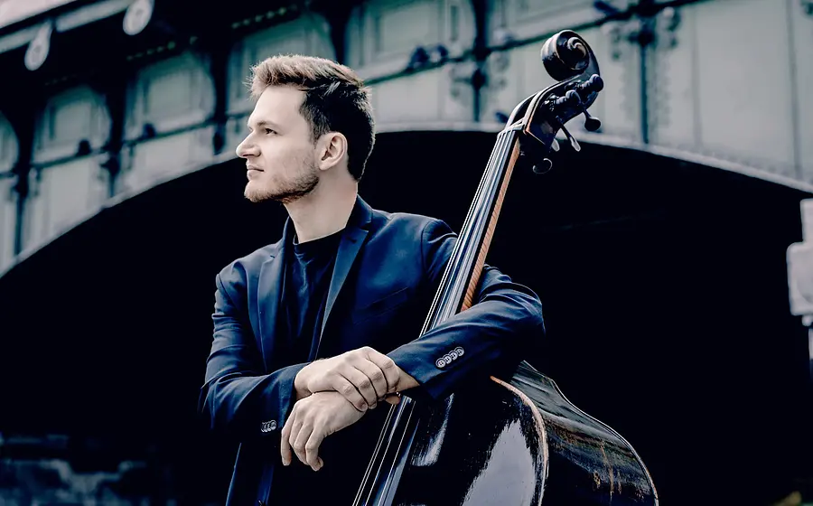 Dominik Wagner lehnt an einem Kontrabass. Im Hintergrund spannt eine Brücke.