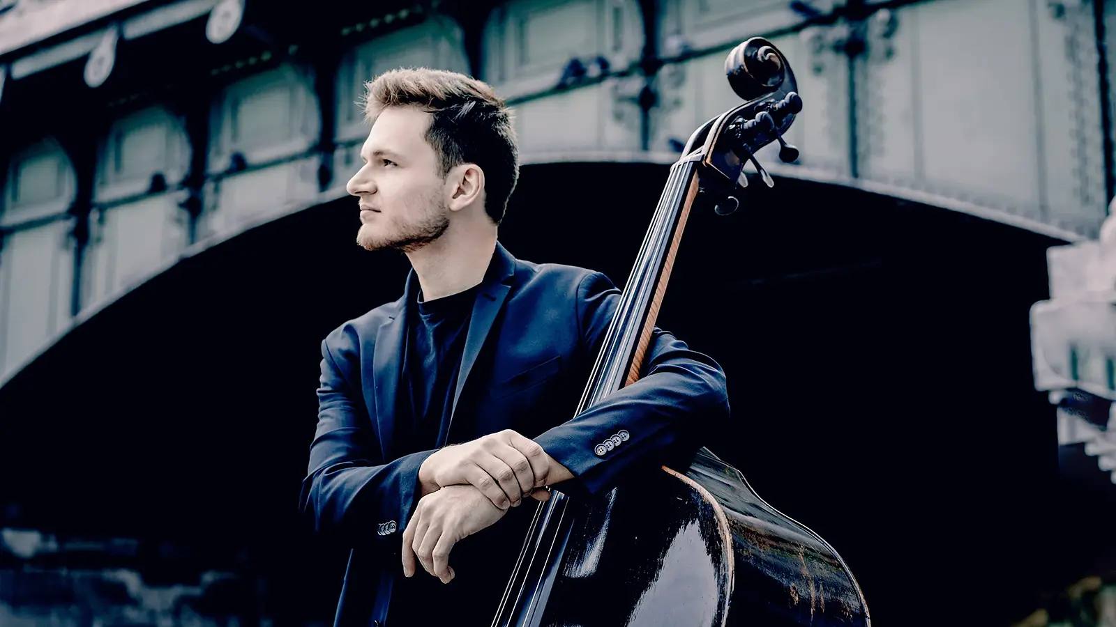 Dominik Wagner lehnt an einem Kontrabass. Im Hintergrund spannt eine Brücke.