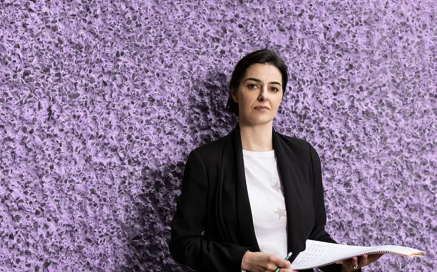 Eine Person in weißem Shirt, schwarzem Blazer mit Notenblatt in den Händen vor violetter rauher Steinwand zur Veranstaltung KOMPONISTENPORTRÄT DOBRINKA TABAKOVA