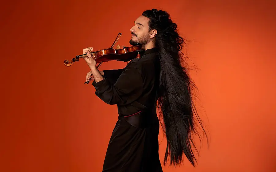 Nemanja Radulovic spielt Violine vor orangefarbenem Hintergrund mit langem, nach hinten fallendem Haar und schwarzer Kleidung.