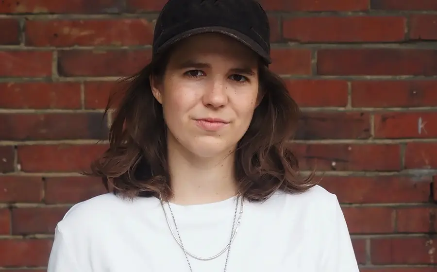 Sophia Merwald mit weißem Shirt und schwarzer Kappe vor einer Ziegelwand