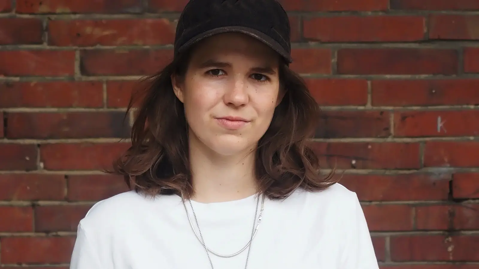 Sophia Merwald mit weißem Shirt und schwarzer Kappe vor einer Ziegelwand