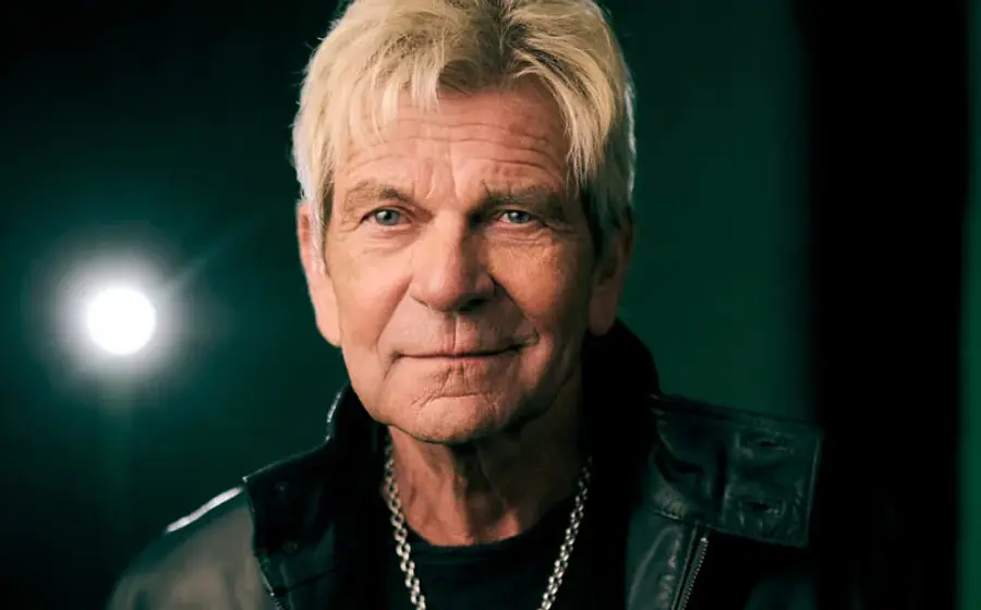 Portrait von Matthias Reim mit schwarzer Lederjacke und Kette vor dunkelgrünem Hintergrund und einem Scheinwerfer, der sich spiegelt