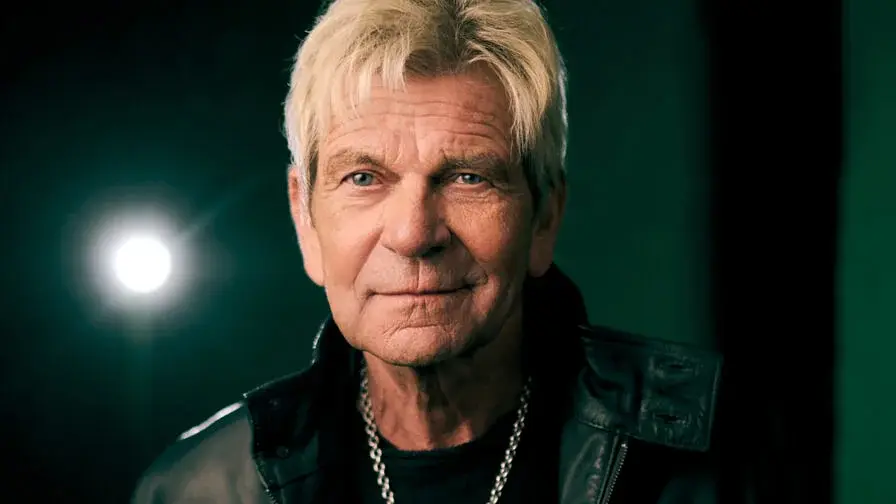 Portrait von Matthias Reim mit schwarzer Lederjacke und Kette vor dunkelgrünem Hintergrund und einem Scheinwerfer, der sich spiegelt