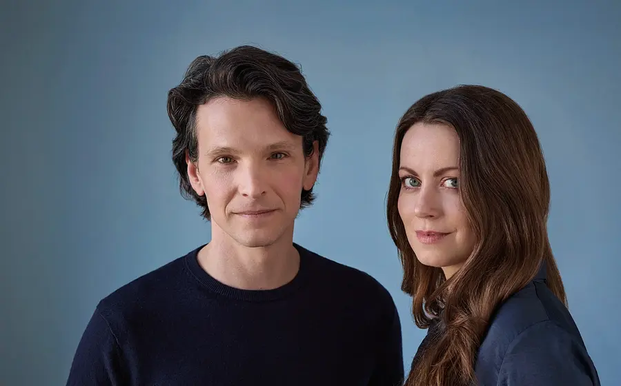 Sabin Tabrea und Alice Dwyer lächelnd  in dunkler Kleidung vor blauem Hintergrund