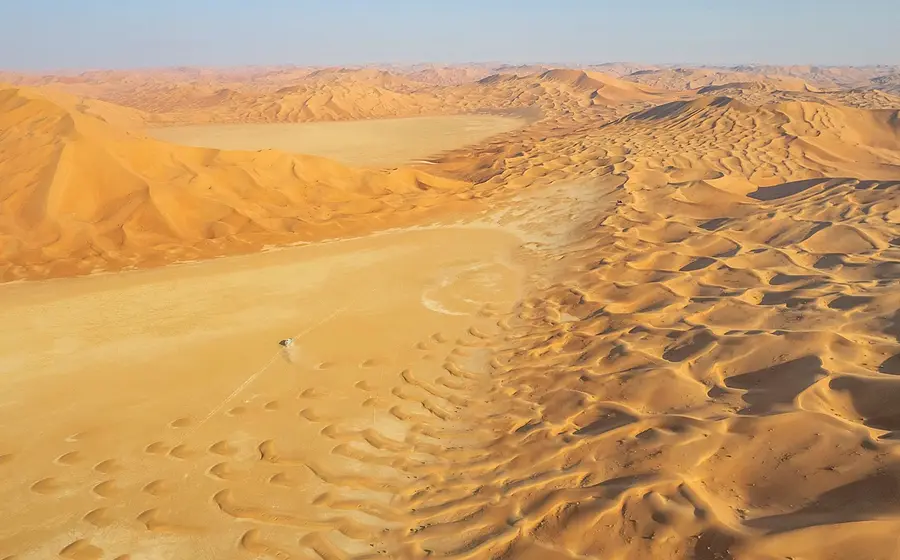 Eine Wüstenlandschaft  mit Sandverwehungen und weit entferntem Horizont und blauem Himmel