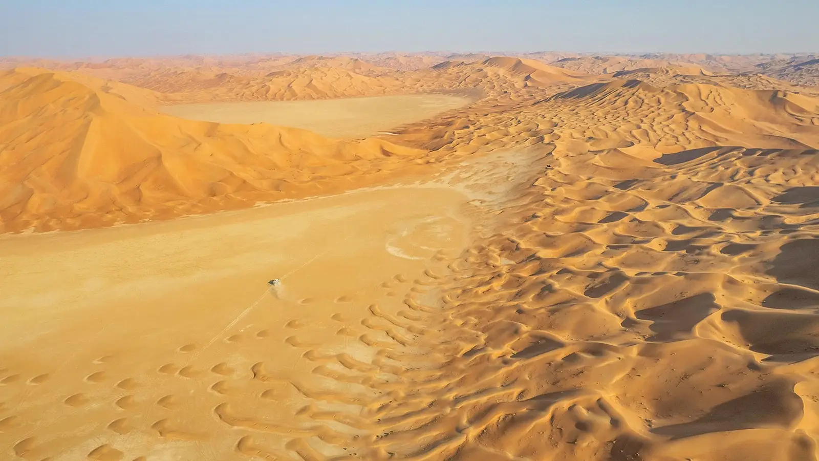 Eine Wüstenlandschaft mit Sandverwehungen und weit entferntem Horizont und blauem Himmel
