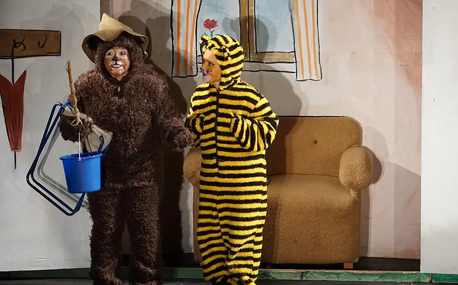 Zwei Darsteller in Kostümen als Bär und Tiger stehen auf einer Theaterbühne mit kindgerechter Kulisse und Requisiten