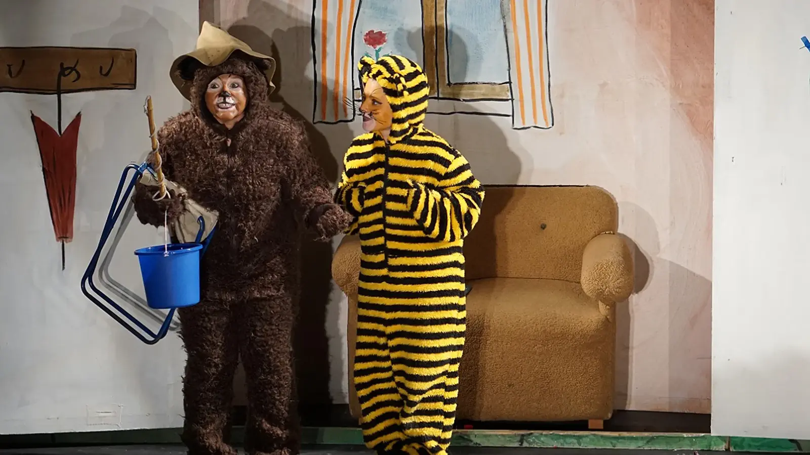 Zwei Darsteller in Kostümen als Bär und Tiger stehen auf einer Theaterbühne mit kindgerechter Kulisse und Requisiten