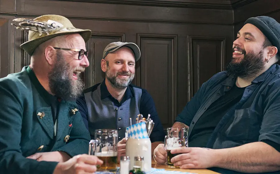 Drei Herren mit Bierkrügen an einem Tisch vor einer dunklen Holzvertäfelung zur Veranstaltung d´Bavaresi