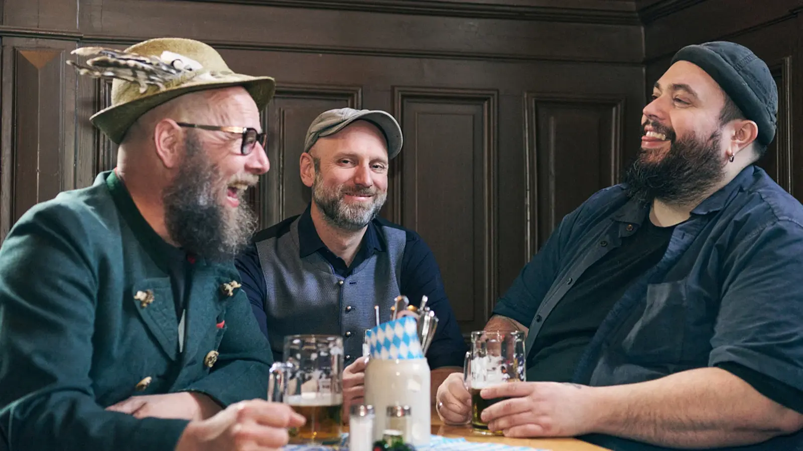 Drei Herren mit Bierkrügen an einem Tisch vor einer dunklen Holzvertäfelung zur Veranstaltung d´Bavaresi