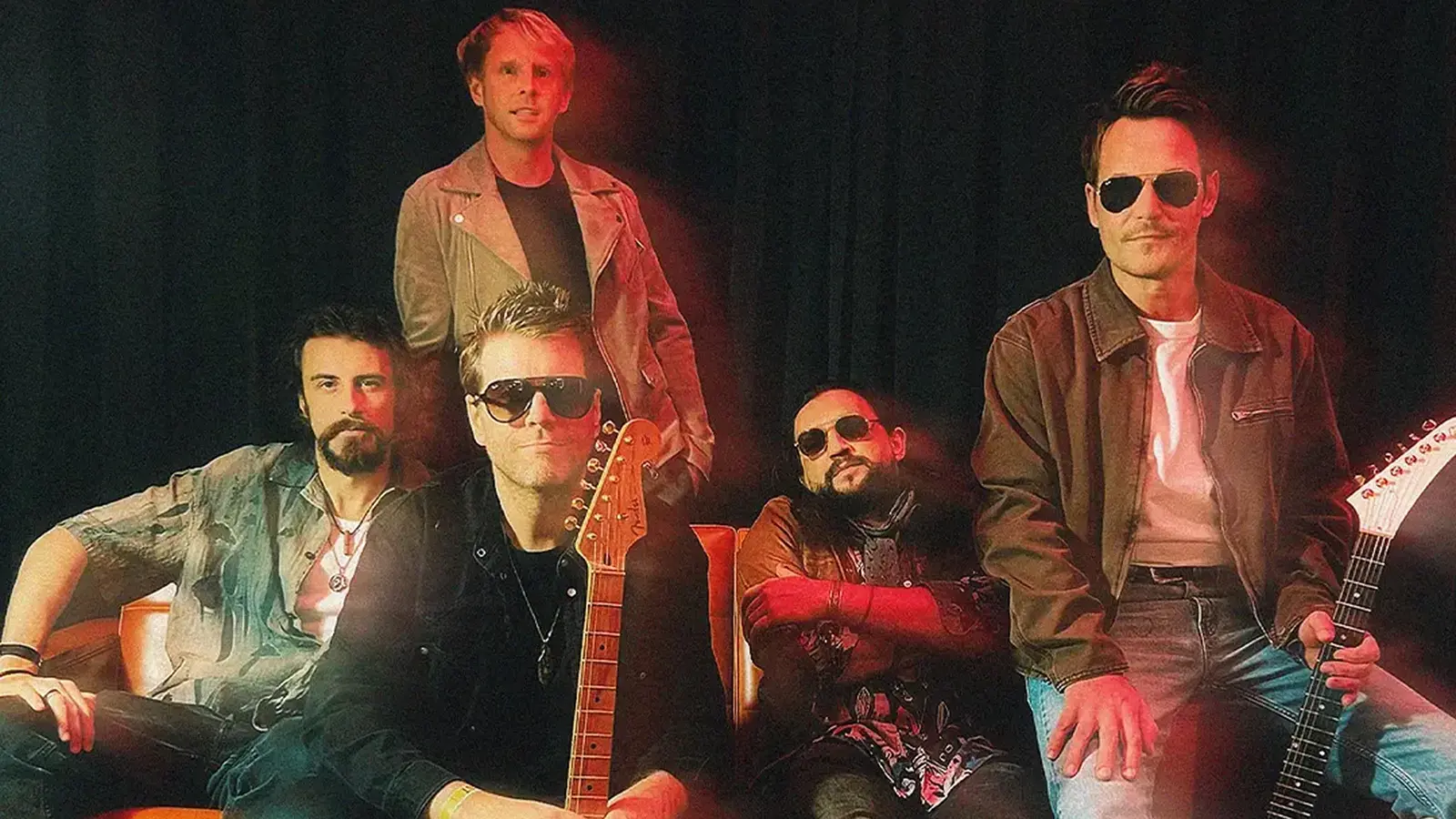 Der Künstler Danny Bryant mit Band auf einem Sofa, einige Personen tragen Sonnenbrillen, in farbigem Scheinwerferlicht vor einem dunklen Vorhang