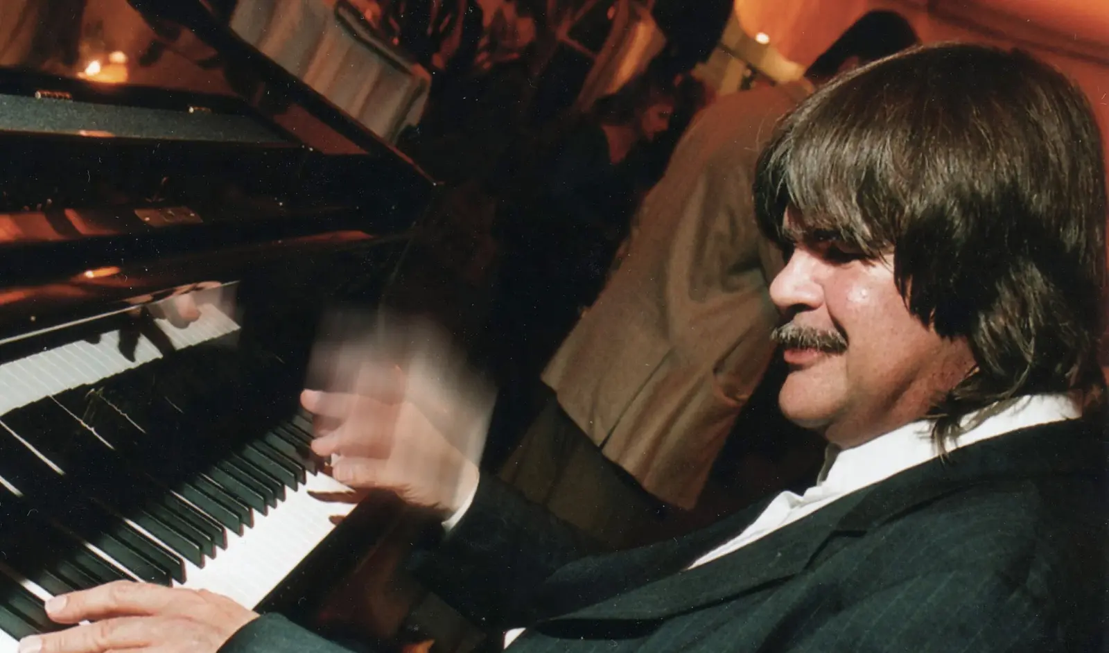 Axel Zwingenberger in schwarzem Anzug spielt am Klavier, eine Hand in Bewegung