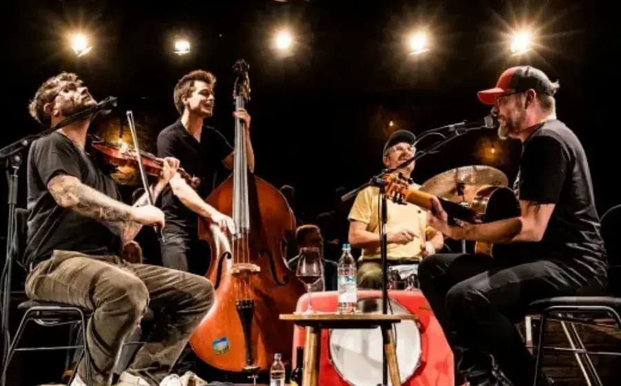 Vier Musiker mit Instrumenten auf Bühne im Scheinwerferlicht