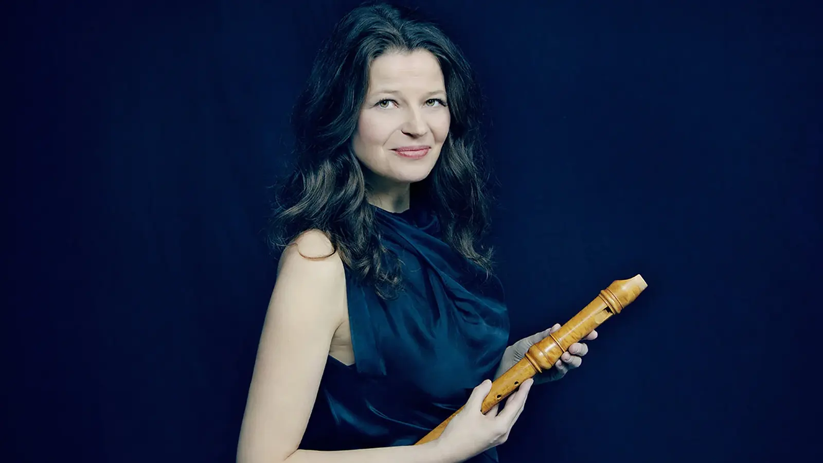 Dorothee Oberlinger mit Flöte in der Hand in einem dunkelblauen Kleid vor dunkelblauem Hintergrund