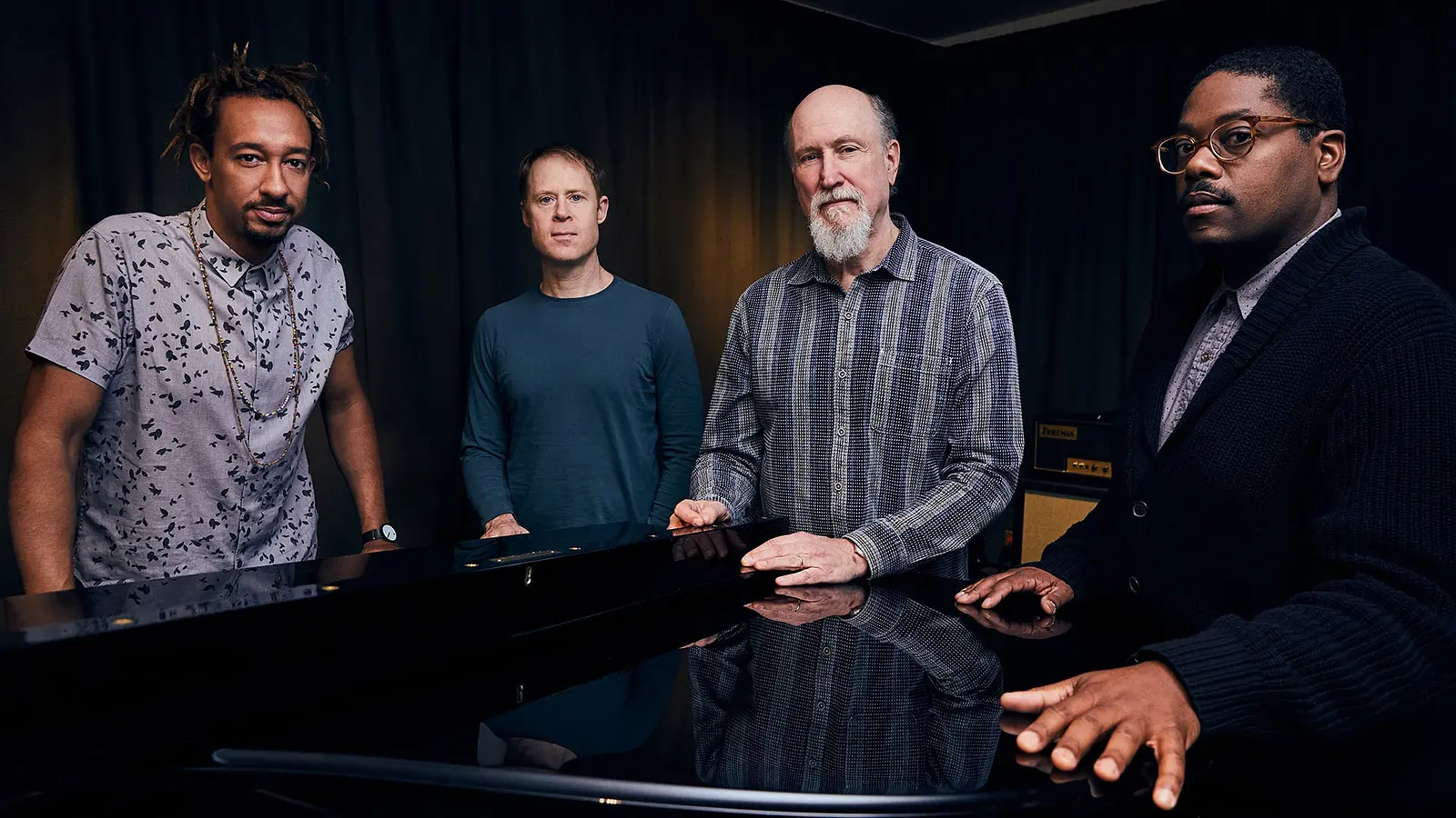 Foto für das Event John Scofield Combo 75 mit der Gruppe, die sich an ein Klavier anlehnt.
