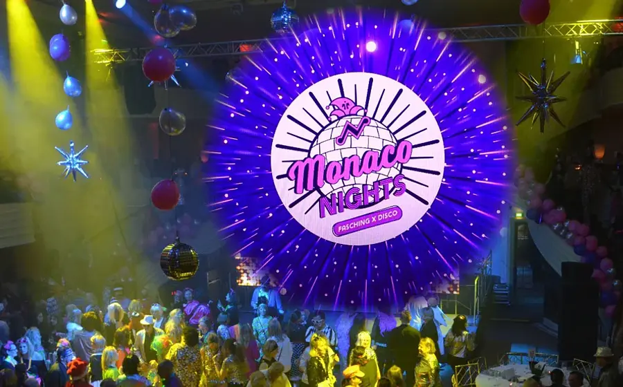 Plakat Monaco Nights mit großer runder Leuchtgrafik in Pink und Violett über einer Tanzfläche voller kostümierter Gäste, umgeben von Luftballons, Discokugeln und bunter Clubbeleuchtung, dazu der Schriftzug Monaco Nights – Fasching x Disco