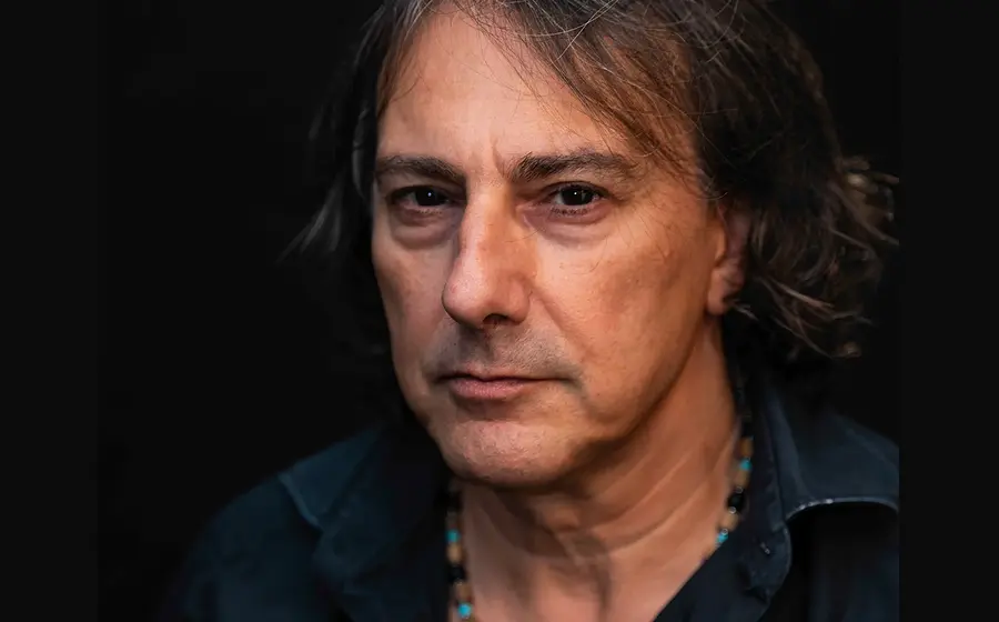 Ein Portrait des Künstlers Pippo Polina in Jeanshemd mit Kette vor dunklem Hintergrund