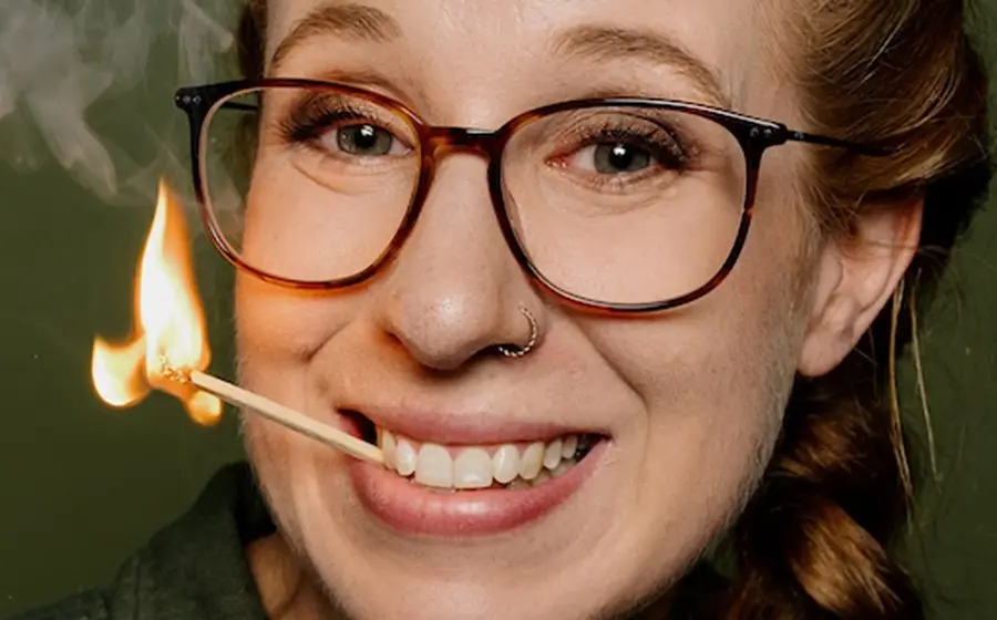 Die Künstlerin mit Brille und einem brennenden Streichholz im Mund