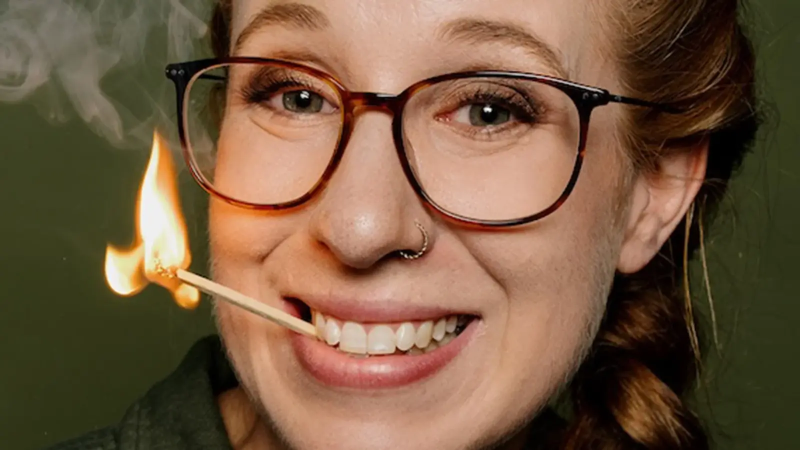 Die Künstlerin mit Brille und einem brennenden Streichholz im Mund