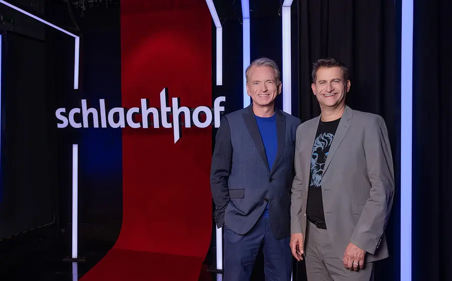 Zwei Moderatoren vor einer Tafel "Schlachthof"