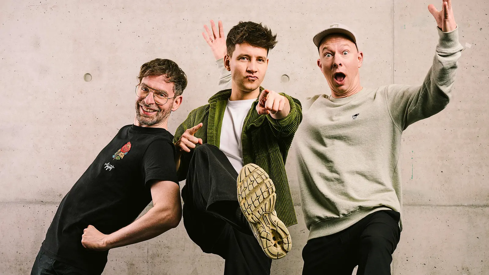 Die drei Bandmitglieder von Deine Freunde in Freizeitkleidung posieren vor einer hellen Mauer