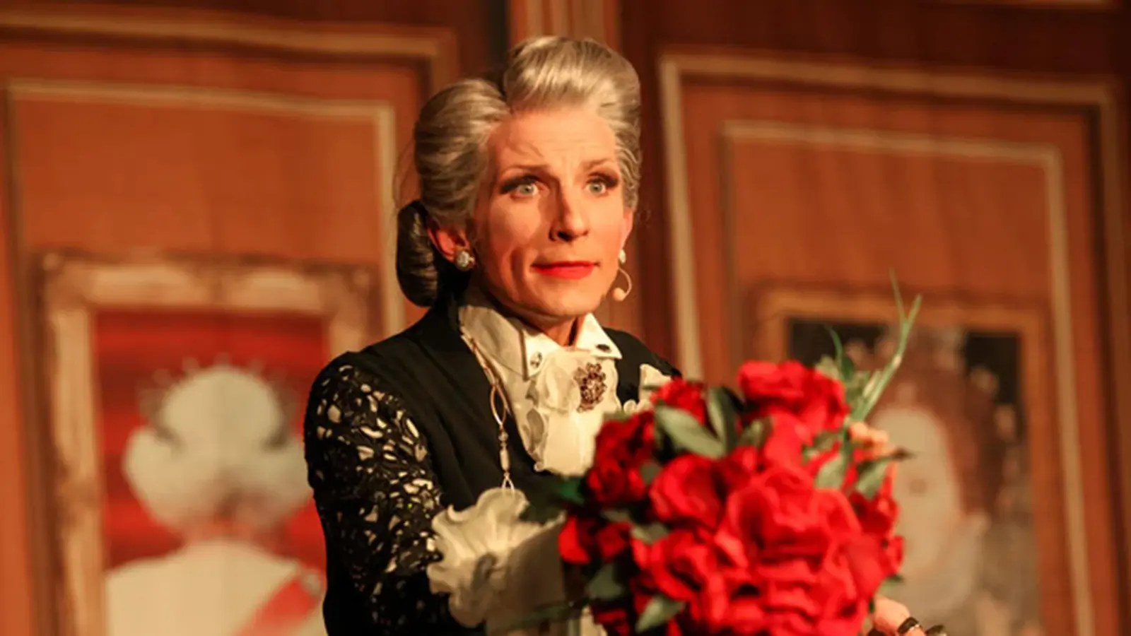 Person in historischer Bühnenkleidung und Hochsteckfrisur mit Blumenstrauß während einer Theateraufführung.