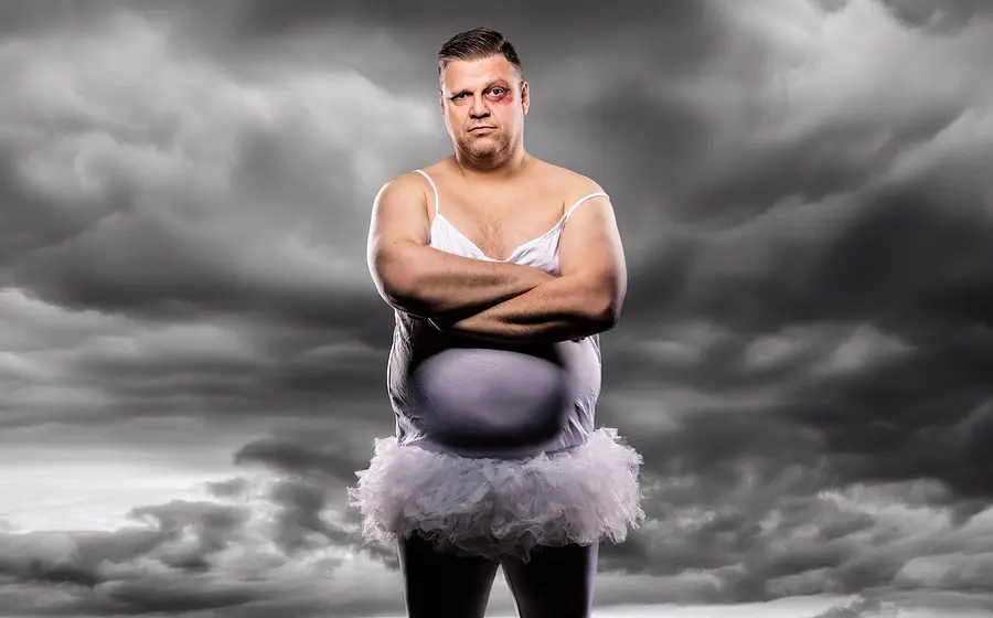 Foto von Ralf Winkelbeiner im fliederfarbenen Kleid mit einem blauen Auge. Im Hintergrund graue Wolken