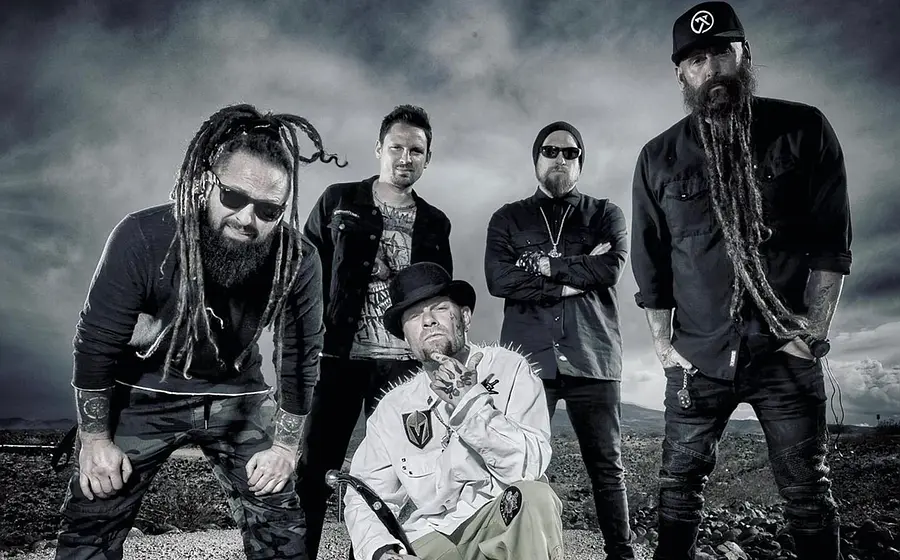 Die Band Five Finger Death Punch in dunkler Kleidung steht im Freien, markanter Himmel im Hintergrund, eine Person mit Hut im Vordergrund
