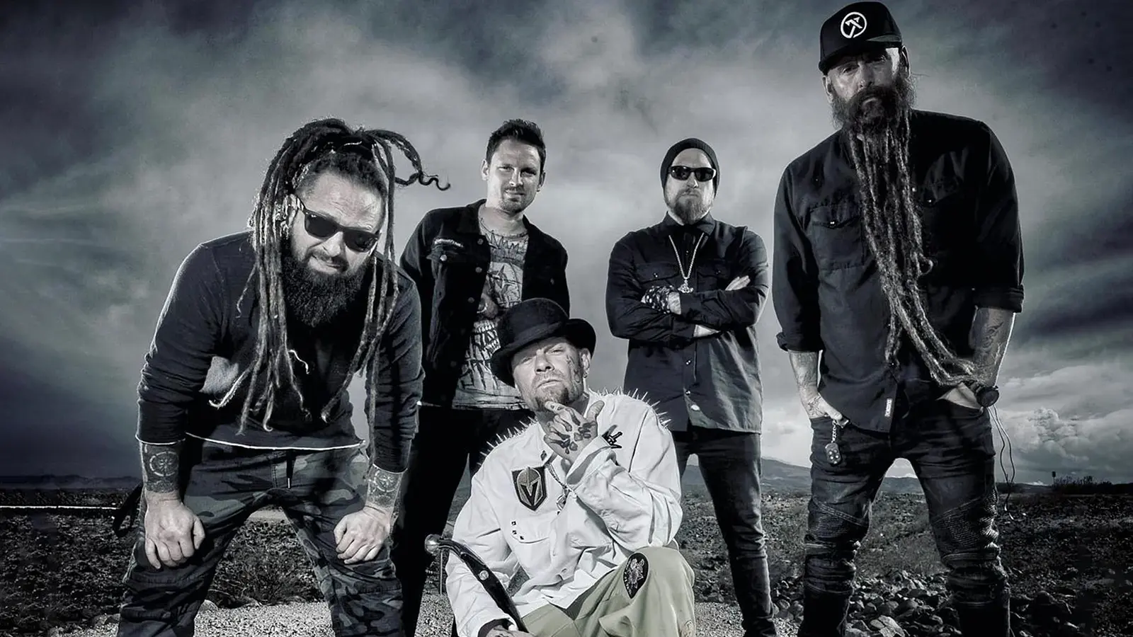 Die Band Five Finger Death Punch in dunkler Kleidung steht im Freien, markanter Himmel im Hintergrund, eine Person mit Hut im Vordergrund