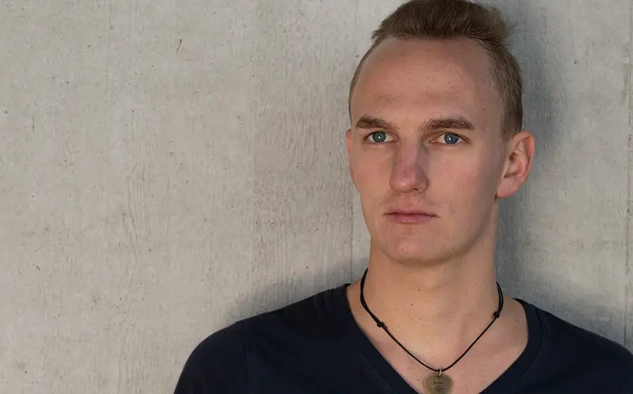 Ein Portrait des Künstlers Frederic Levi in schwarzem Oberteil vor marmoriertem hellgrauen Hintergrund